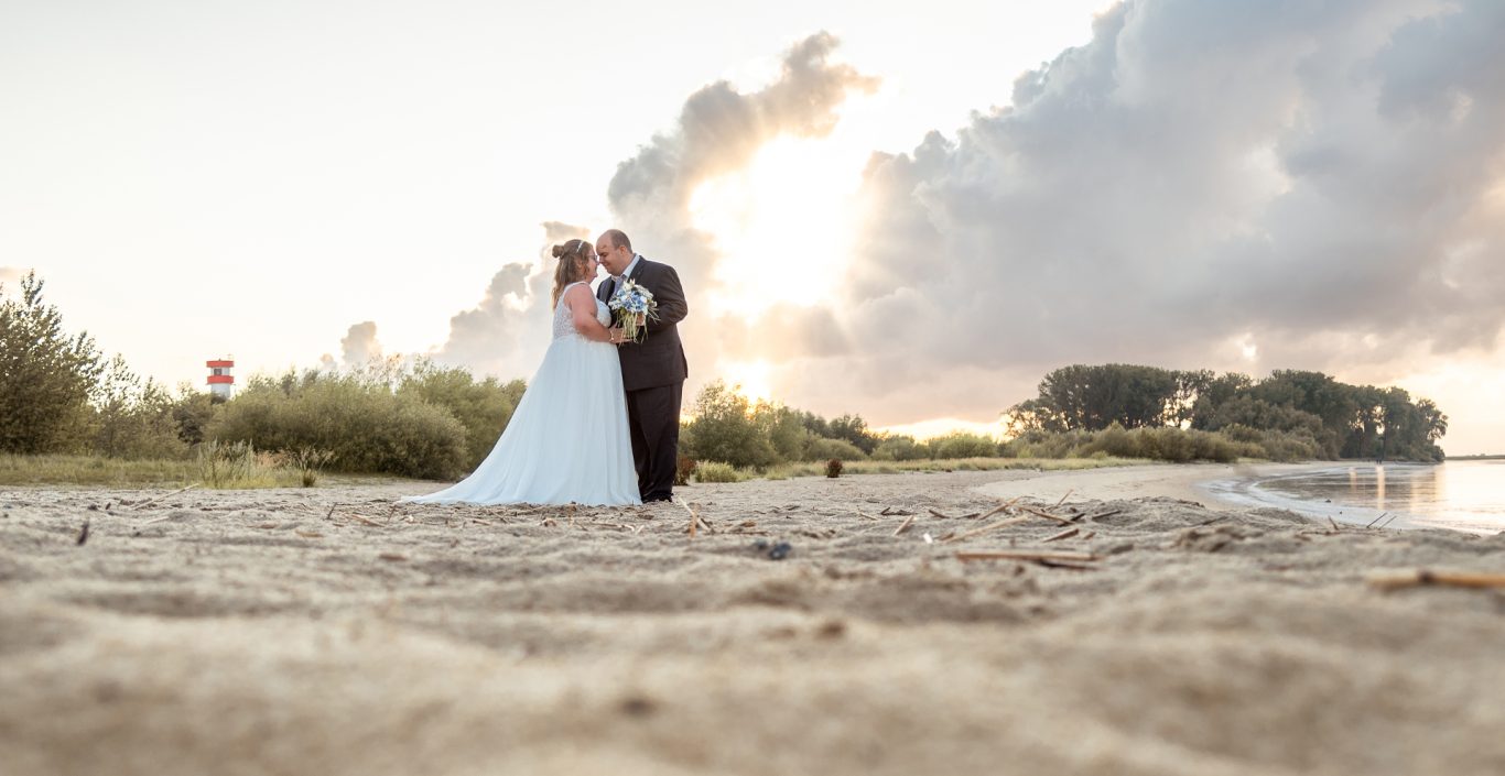 Brautpaar umarmt sich am Strand bei Sonnenuntergang, umgeben von Natur.