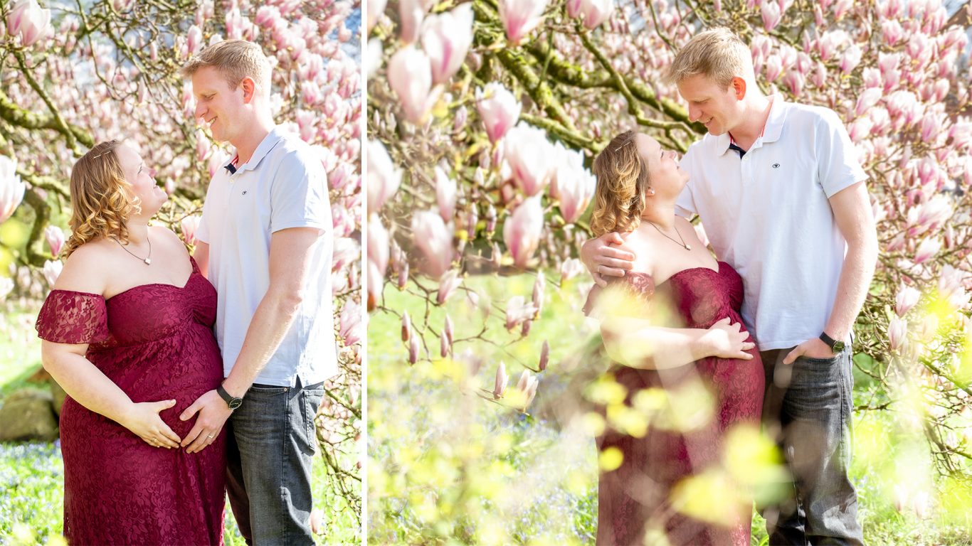 Ein werdendes Elternpaar steht umgeben von blühenden Magnolienbäumen.