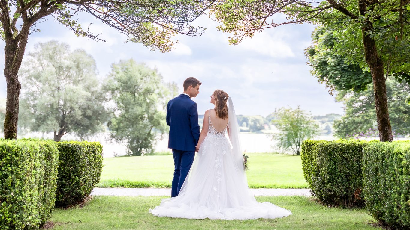 Das Brautpaar steht Hand in Hand vor einer malerischen Landschaft mit Bäumen.