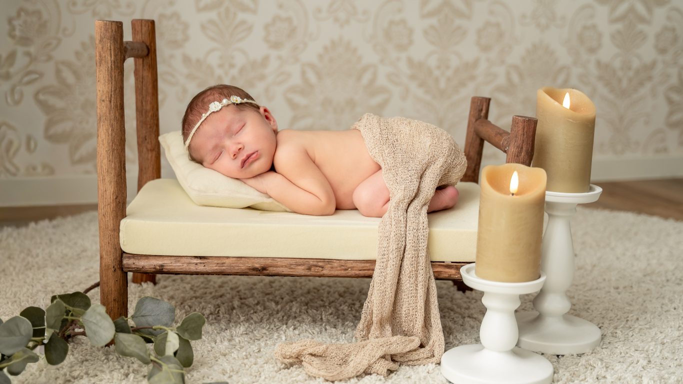Neugeborenes Baby schläft auf einem kleinen Bett umgeben von Kerzen und Dekoration.